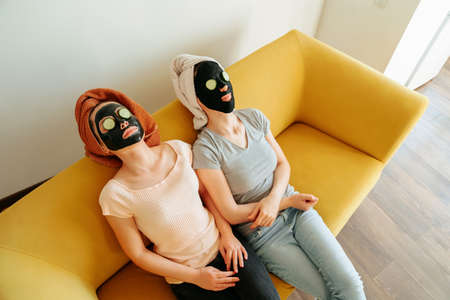 top view of a two young woman lying with cosmetic masks on their faces and cucumber slices on their eyes. side view, Beauty treatmentの写真素材