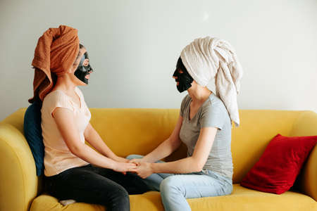 Portrait of pretty joyful girl friends doing beauty treatments at home. Cheerful young women relaxing in living room. Skincare conceptの写真素材