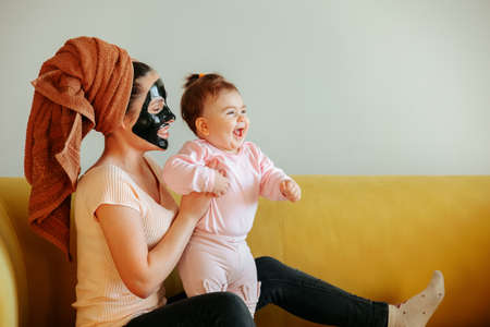 Funny footage of joyful mother and little baby daughter. fun at home mom and baby sitting on the couch during skin care procedureの写真素材