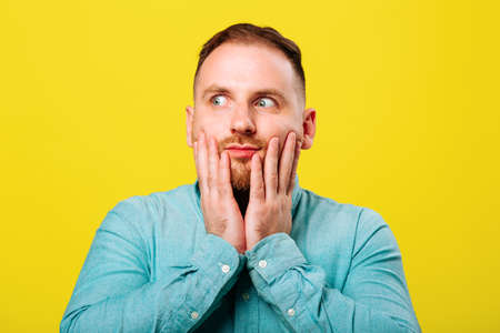 Young handsome man with beard wearing blue shirt over yellow background afraid and shocked, surprise and amazed expression with hands on faceの写真素材