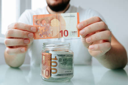 Cropped view of male hand putting euro banknote into glass jar. man saving in jarsの写真素材
