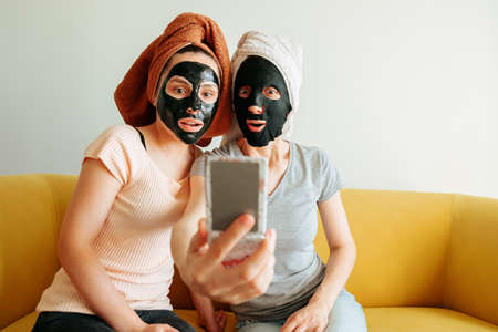 two girls with cosmetic masks, scared, look in the mirror. skin care, shocked or surprised, scary chemicals in beauty products. at homeの写真素材