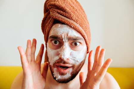 shouts, scared and messy man applying beauty facial mask looking at camera surprised and horrified. male cosmetic face treatmentの写真素材
