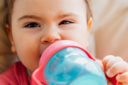 funny baby drinking bottled water. baby girl sitting in a child seat and holding a bottle of water in her hand.の写真素材