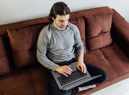 Work from home, home office. A young guy in casual clothes is using laptop for online communication. He sitting on sofa, looks at the laptop screen and speaksの写真素材