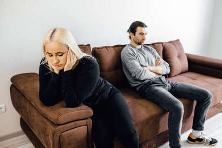 Unhappy young wife and husband not talking after quarrel, sitting on couch at home separately back to back, upset couple ignoring each other, relationships conflictの写真素材