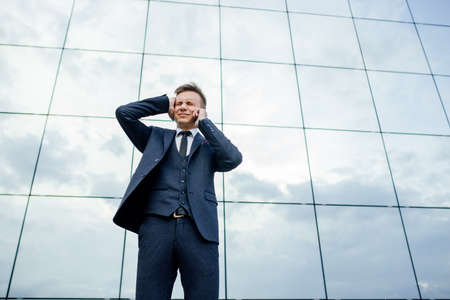 Low angle view of a angry young businessman talking on smartphone in city outdoors. standing over business center backgroundの写真素材