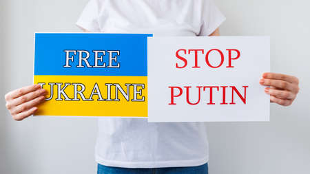 close up of a Protester hands holding cardboard Banner with the words stop putin free ukraine. protesting against the Russian invasion. banner inscription cardboard massage Hands Off Ukraine.の写真素材