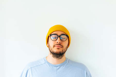 front view of a portrait of a bearded man and eyeglasses. male with closed eyes and yellow hatの写真素材