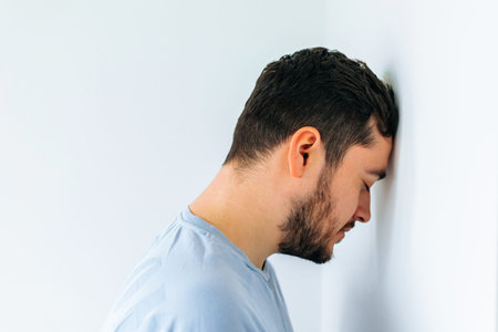 Side view of an unhappy man resting head against office wall. worker banging his head against the wall in despair. Male head against wallの写真素材