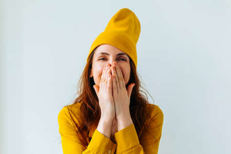 smiling hipster girl teenage girl He covered his face with his hands with yellow hat on her head, looking at the camera and smiling slightly.の写真素材