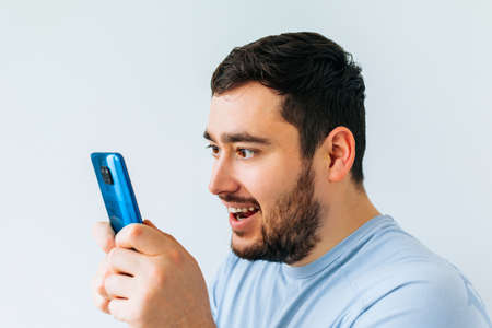 Portrait of a joyful young man holding smartphone. bearded Smiling young man holding smart phone and looking at it. Portrait of a happy man using mobile phoneの写真素材