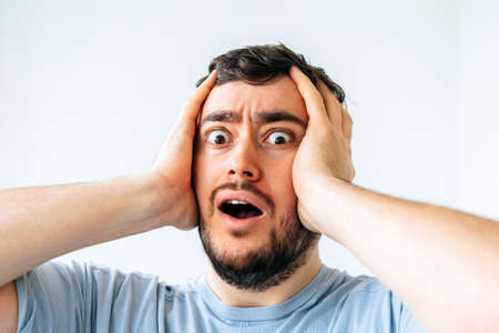 Beard man wonder, wearing casual t-shirt standing over isolated white background afraid and shocked with surprise expression, fear and excited face. Man looking at camera with surprised expressionの写真素材