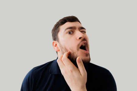 Young man scratching bearded, Bearded guy scratching his beard. In the studio on a gray background. thoughtful gesture, indoors studio shotの写真素材
