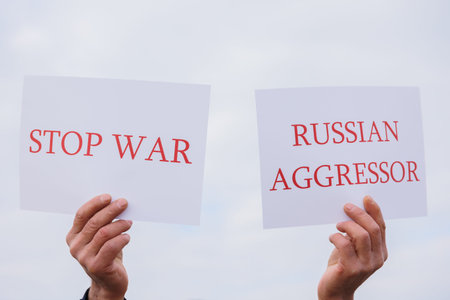 close up of a Protester hands holding cardboard Banner with the words russian aggressor, stop war on...