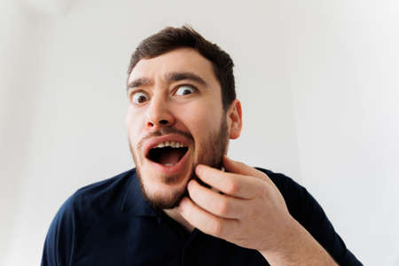 Portrait of a stylish young man scratches his beard and screams in pain. Annoying itch, beard itchingの写真素材