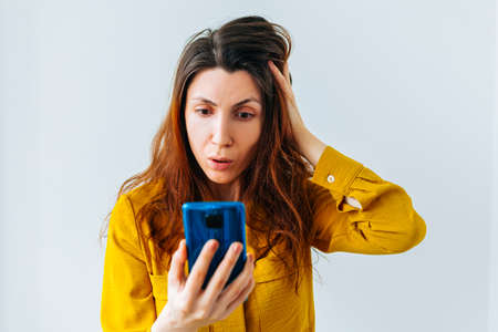Worried woman looking at smartphone with ruffled and dirty hair. the concept of hair care and remote discussionの写真素材