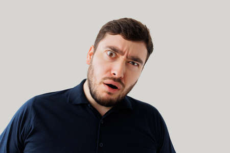 Bearded young man is surprised and dumbfounded, he looks at the camera with a stupid expression on face. man with intense expressionの写真素材