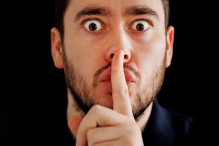 Censorship concept, Secret information. Mysterious bearded man looking at camera and putting finger on lips. isolated on a black backgroundの写真素材