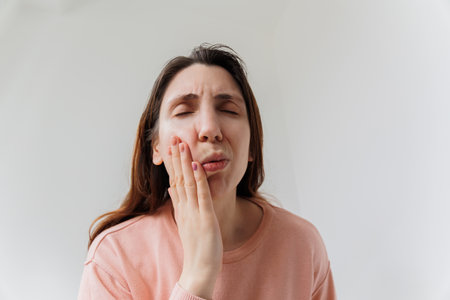 Handsome bearded woman suffering from toothache, closeup, touching his cheek to stop pain against white background. painful expression because of toothache or dental illness on teeth.の写真素材