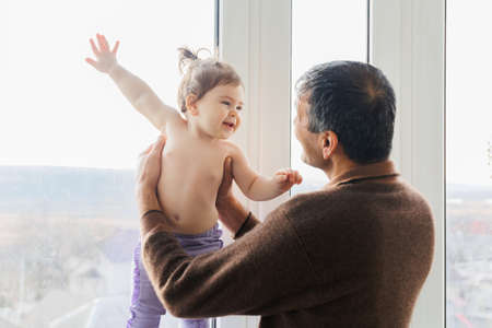 Senior elderly man playing to his baby granddaughter, holding him in the air. Two age generations family old grandparent and small grandkid enjoying activity together.の写真素材