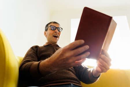 old indian man reading a book at home wearing glasses scared in shock with a surprise face, afraid and excited with fear expression. Senior Male Read Book, Amazing Face Crazy Shocked Eyesの写真素材