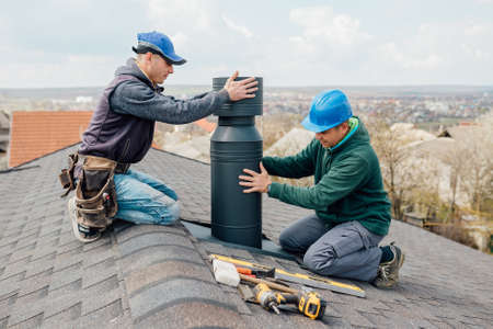 two Professional workmens standing roof top and measuring chimney of new house under construction against blue backgroundの写真素材