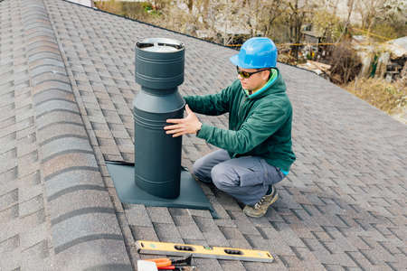 worker with blue helmet on the roof installing iron chimney. roofing Construction and Building New iron House with Modular Chimney.の写真素材