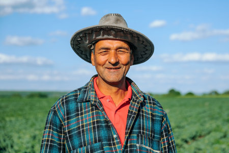The portrait of a male farmer in a plaid shirt with a hat on his head is satisfied with the agricultural field. Slow moving portrait of old farmer looking at camera after a beautiful days work.の写真素材