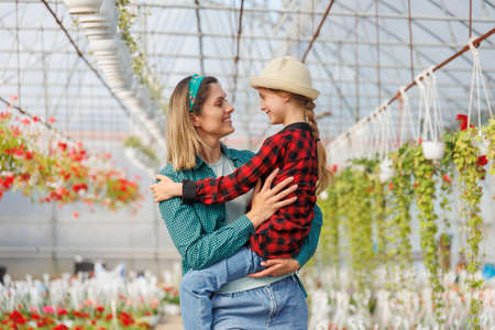 happy gardeners family kid girl with her mother, mother holding her daughter in her arms, looking at each other, they are happy and spending time together. the greenhouse background, copy spaceの写真素材