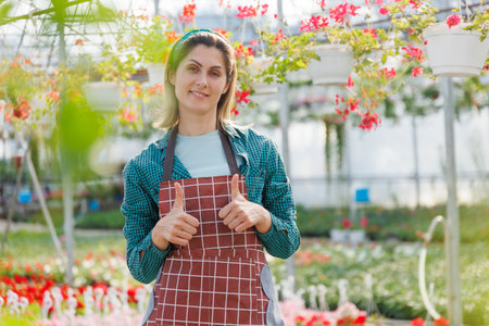 woman entrepreneur gardener with the thumb up, it shows the ok sign posing in greenhouse. joyful female she is confident and satisfied with the small businessの写真素材