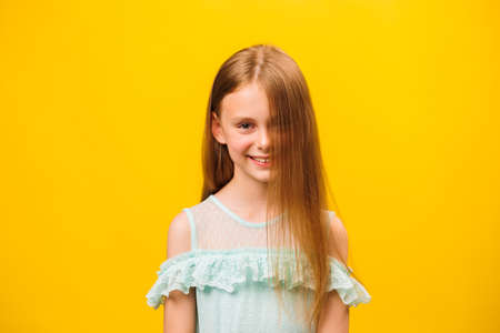 portrait of child Caucasian girl looking looking at camera and smiling. front view, smiley kid face against a yellow backgroundの写真素材