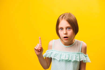 idea, surprised amazed little americana children girl pointing finger up over yellow background. kid warning and childhood concept, copy spaceの写真素材