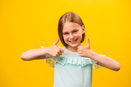 Like and approval. Studio portrait of stylish little children girl gesturing thumbs up and looking at camera. smiling to camera, yellow backgroundの写真素材
