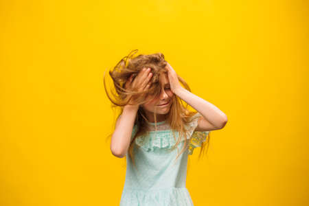 disheveled, kid girl scratch hair on the yellow background, studio shot. scalp problems, tousled and dirty hairの写真素材