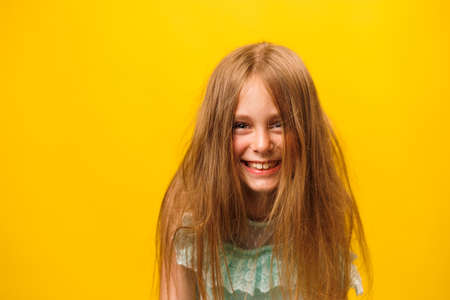 front view portrait of smiling preteen children girl with messed hair, isolated on yellow background. Beautiful happy child looking at camera and with disheveled hair on head. Hair care.の写真素材