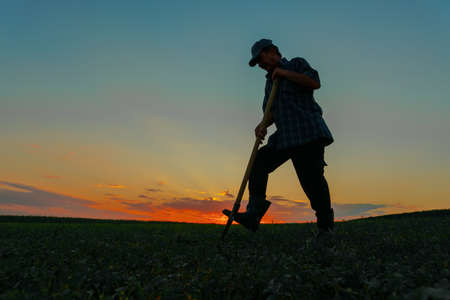 the silhouette of a peasant man working digging on agricultural land at sunset against the background of dramatic colorful sky.の写真素材