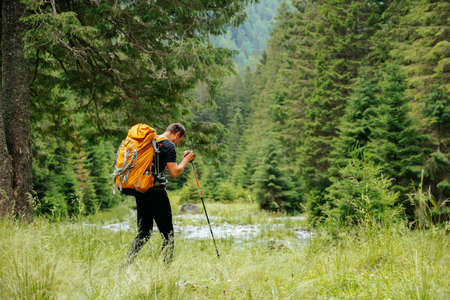 front view of caucasian american man outdoors hiking using walking poles in countryside, male tourist looking away active lifestyle travel adventure vacations sunsetの写真素材