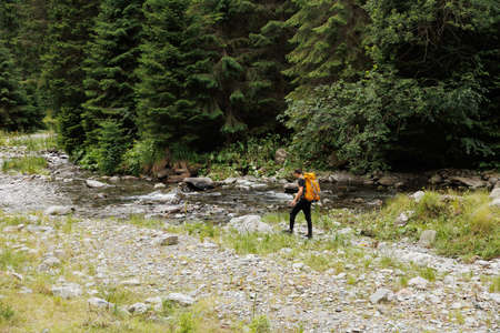 rear view of a tourist young man with a backpack travels through the forest near the river. young man equipped with tourist equipment hiking, lifestyle. active life mode, active restの写真素材