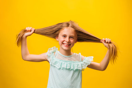 Portrait of a happy cute funny girl. The child holds the hair with his hands. Standing on a yellow...