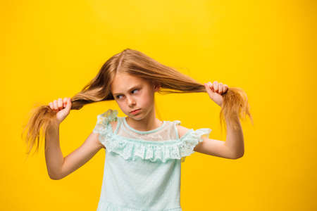 Artistic girl shows her emotions. The child stands on a yellow background, in a beautiful turquoise dress. Kid holds hair with hands. child and copy space. yellow backgroundの写真素材