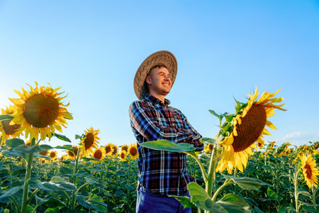 side view of Happy lucky young farmer with arms crossed stands in his field with sunflowers. Man...
