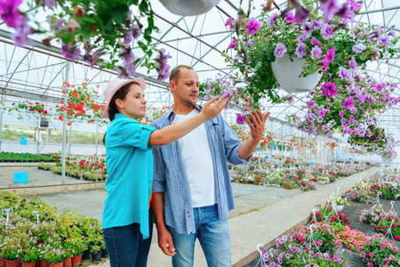 Young gardeners standing in greenhouse with flowers, they are looking at flowers, smiling happily....