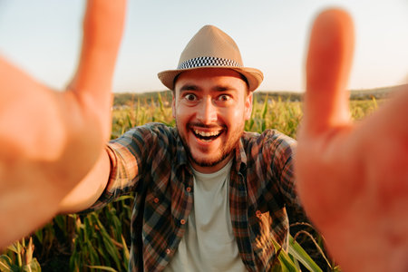 Close up crazy emotion of a young farmer man in a hat, hands, unrealistically crazy joy standing in field. Looking at camera. The farmer in the field after the worker resets emotions.の写真素材