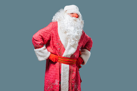 Santa Claus with an attentive tired look stands swaying on blue background, red nose, white fluffy beard. Father Frost has a lot of work, Christmas and New Year worries. Front view looking at camera.の写真素材