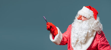 Santa Claus with a red nose on a blue background side view stands on the right and show to the left with a pointer. A look to the side. Serious Santa showing something. Copy space. Blue isolated.の写真素材