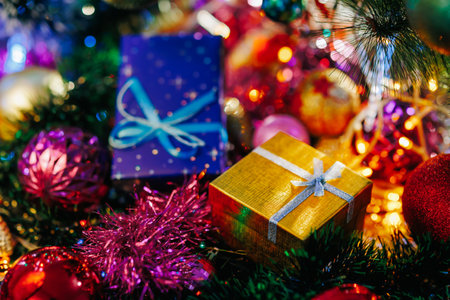 A garland on a Christmas tree shines beautifully in different colors, a close up of a golden gift box. Blurred background of Christmas decorations, soon the new year. Selective focus.の写真素材