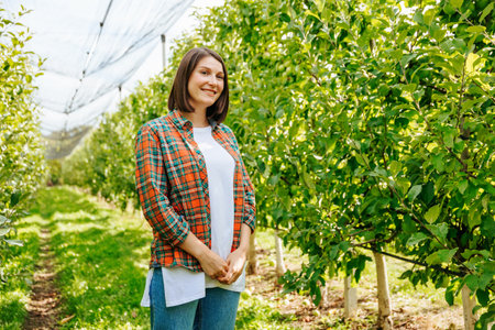 Front view young woman farmer calm smile stands with her hands clasped in castle apple orchard looking at camera. The concept of farming and family business. Happy woman with short haircut. Copy spaceの写真素材