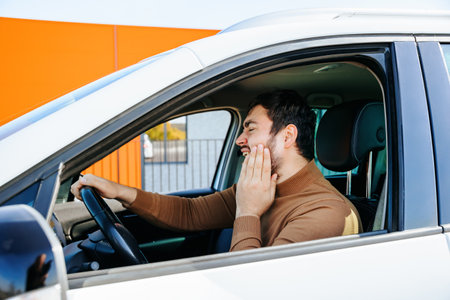 bearded driver is worried, he has toothache inside the vehicle behind the wheel. nice man with hand on face is irritated dental pain, The guy suffers from pain in the mouth and presses his handの写真素材