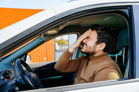 people and ache migraine and headache tired and unhappy man. American man inside the car holds his head with his hand, negative emotionsの写真素材